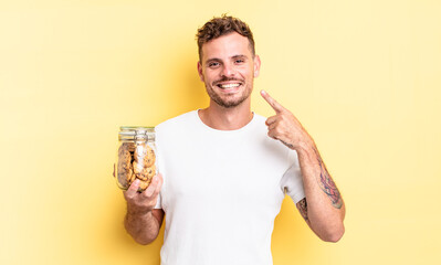 young handsome man smiling confidently pointing to own broad smile cookies bottle concept