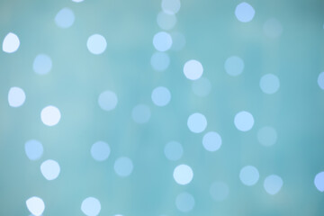 Blurred view of festive lights on light blue background. Bokeh effect