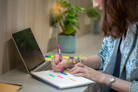 Asian student does her homework and writes down calendar dates while studying online at home.