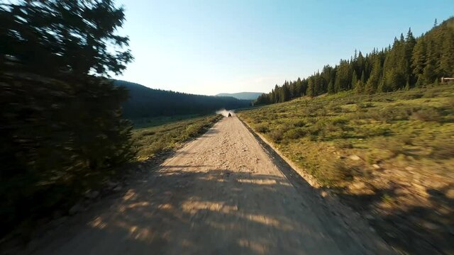 FPV drone flying towards and passing motocross ATV on dusty road in sunset