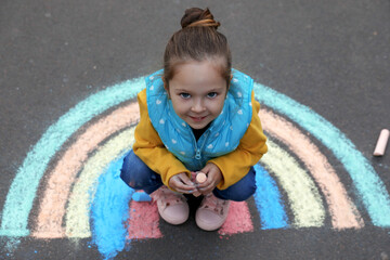 Fototapeta premium Happy child near chalk drawing of rainbow on asphalt, above view