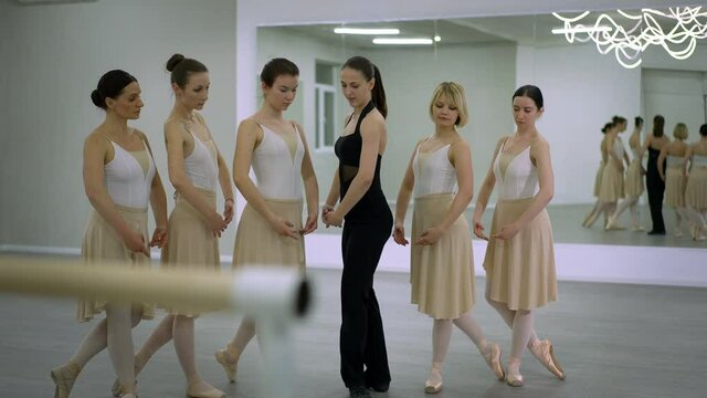 Slim beautiful Caucasian woman teaching ballet showing position talking walking in studio with group of students standing indoors. Professional ballerina rehearsing movements with dancers
