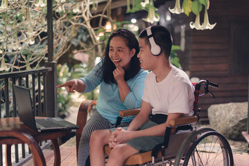 Obraz premium A woman smiling face using computer for video chat and social media with her son, Blur of a person with disability in wheelchair, Hobby and family life in sweet home concept.