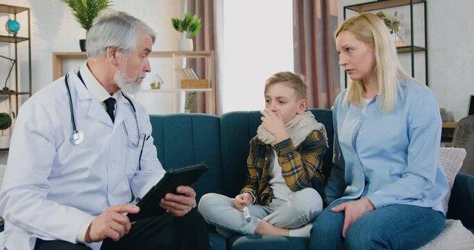 Beautiful caring loving blond woman sitting near her sick tired son which talking with respected attantive high-skilled bearded doctor when he visiting them at home,medicine and healthcare concept
