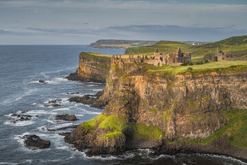 Dunluce Castle illuminated by sunlight, perched on the edge of cliff, Bushmills, Northern Ireland....