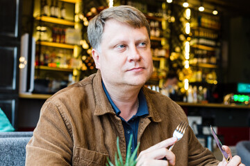 Fototapeta premium An adult blond man having lunch in a cafe in brown jacket.