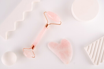 Pink face roller and gua sha massager made from natural  quartz  stone over white background.  Lifting and toning treatment at home.