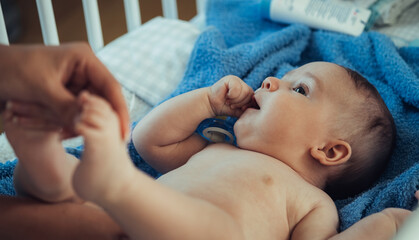 Unrecognizable Mother Wrapping her Clean Baby Boy in a Towel After Bath at Home. 

An anonymous mother hands drying her cute baby with blue towel on a baby bed.