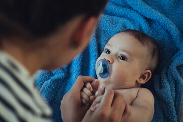 Baby Boy whit Pacifier Lying on a Towel Clean After Bath at Home. 

Close up photo of an anonymous mother applying skin care moisturizing cream on her cute baby on a baby bed.
