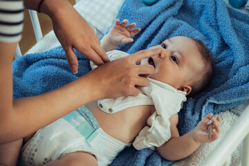 An Anonymous Mother Having Fun while Dressing Up her Little Baby Boy in a Bed. 

Unrecognizable mother touching nose of her adorable newborn baby who is lying on a bed and getting dressed. - Powered by Adobe