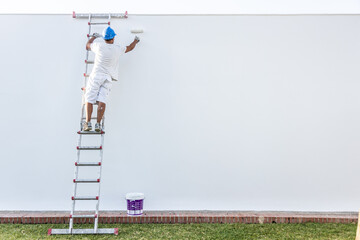 Back view of a young painter painting on a ladder