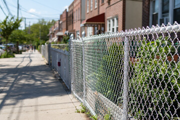 Chain Link Fence along an Empty Sidewalk with a Row of Old Homes in Astoria Queens New York