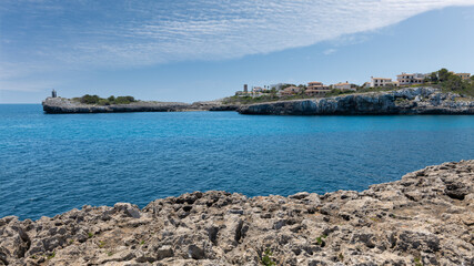 The entrance to the natural harbor Porto Cristo on the Spanish Mediterranean island of Mallorca. There is a tower on the opposite side. There are rocks in the foreground.