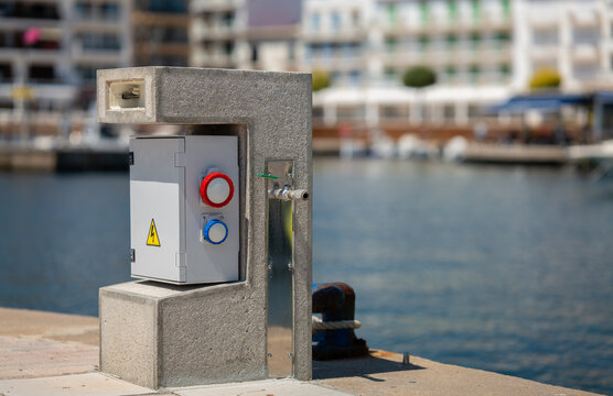 A box for power connection in a small yacht harbor on the Spanish island of Mallorca. Behind it are bollards where boats can moor. There is a tap on the side.