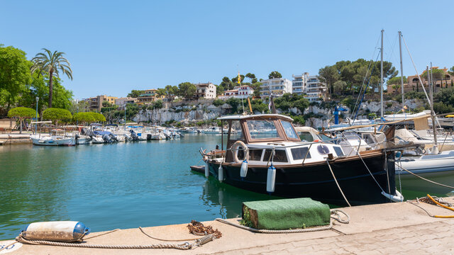 The small marina in the natural harbor of Porto Cristo on the Spanish Mediterranean island of Mallorca. Motor and sailing boats are moored. There are beautiful houses upstairs.