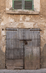 Fototapeta na wymiar An old front door on a house in the old town of Felanitx on the Spanish island of Mallorca. The door is made of wood and has been repaired several times. There is an old window upstairs.