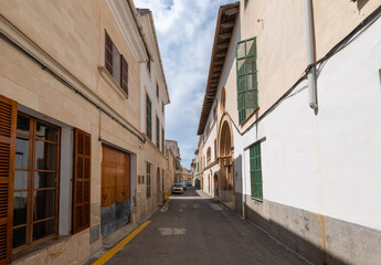 Fototapeta na wymiar A narrow street in the old town of Felanitx on the Spanish island of Mallorca. Some cars are parked in front of the houses. The sky is blue with beautiful clouds.