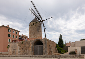 The old historic windmill in the town of Llucmayor on the Spanish Mediterranean island of Mallorca. The substructure is made of stones. There are clouds in the sky.