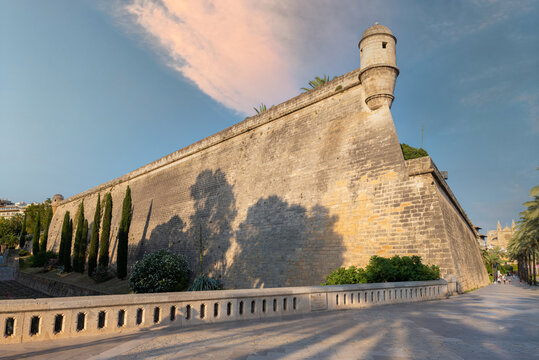 The old fortress Baluarte at the port of the city of Palma on the Spanish island of Mallorca. There are high walls. On the right is the promande and on the left are beautiful trees.