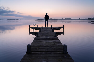 A man looking over a lake during a foggy, tranquil morning.