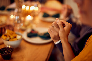 Close-up of couple hold hands while saying grace during Hanukkah meal.