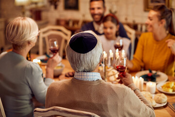 Rear view of Jewish senior man during family lunch at dining table on Hanukkah.