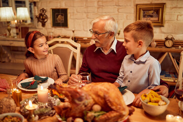 Happy kids talk to their grandfather during family lunch on Thanksgiving.