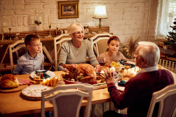 Happy grandparents enjoy in Thanksgiving meal with their grandkids at dining table.