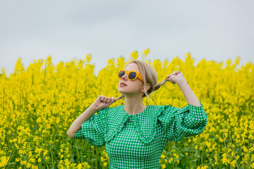 Beautiful blonde in yellow sunglasses and green dress on yellow rapeseed field