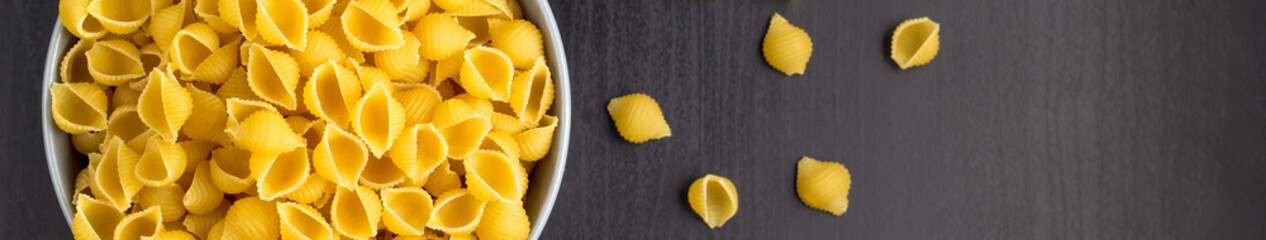 banner of Top view of black background with italian raw conchiglie paste shells in bowl with copy space