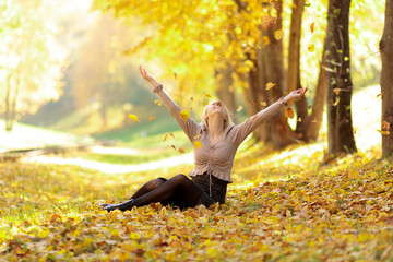 blonde girl in street clothes sitting in a heap of autumn leaves