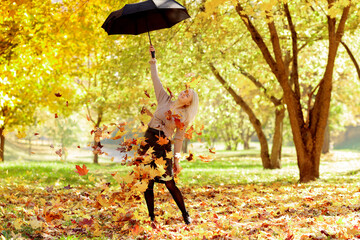 Young woman in the park sprinkles autumn leaves on herself from an umbrella