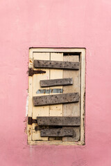 Drewniane okno zabite deskami, na tle różowej ściany, domu.