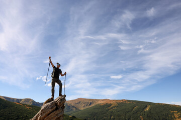 Man with backpack and trekking poles on rocky peak in mountains