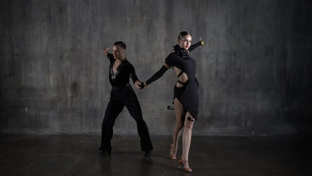 Young elegant girl and boy dance ballroom couple in black dress dancing tango in sensual pose over grunge background. Professional dancers perfoms latino. Human emotions, love and passion