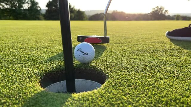 Putting a golf ball into the hole on a perfect golf green with a setting sun