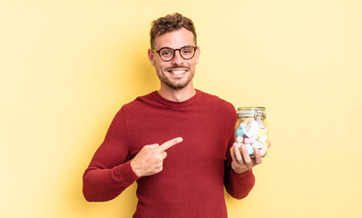 young handsome man smiling cheerfully, feeling happy and pointing to the side. jelly candies concept - obrazy, fototapety, plakaty