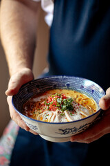 Chef holding a bowl of japanese curry chicken ramen with tomatoes