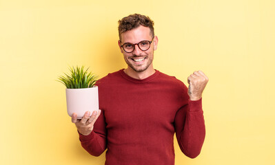 young handsome man feeling shocked,laughing and celebrating success. decorative plant concept