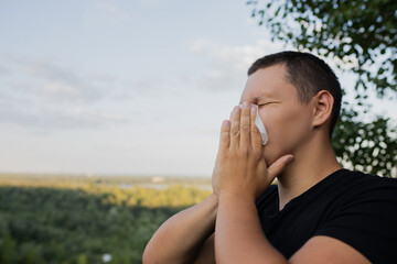 A man in a black T-shirt is wearing a handkerchief on the street. the man sneezes.