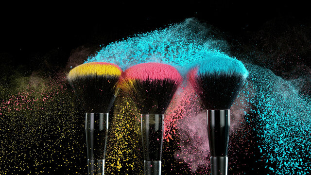 Soft cosmetics brush releasing a cloud of colored face powder.