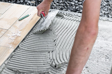 The hands of the tiler lying or installing modern, ceramic tile above cement on the garden terrace...