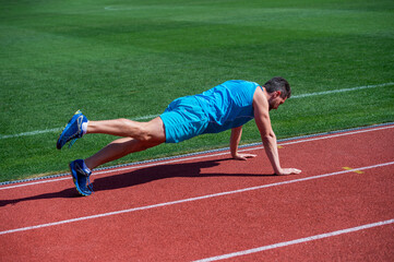 athletic muscular man doing plank outdoor on stadium, core