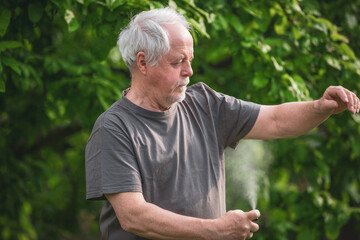 Senior man spraying or using repellent against kind of insects, mosquitoes and ticks in the forest, protective spray, healthcare concept