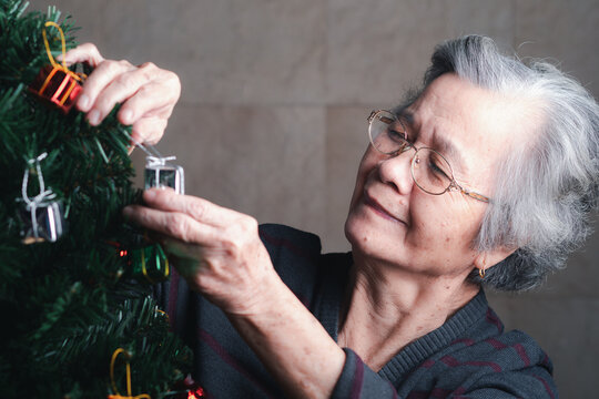 Happy senior woman decorating the Christmas tree while sitting in a living room at home. Space for text. Concept of aged people and Christmas and happy new year festival