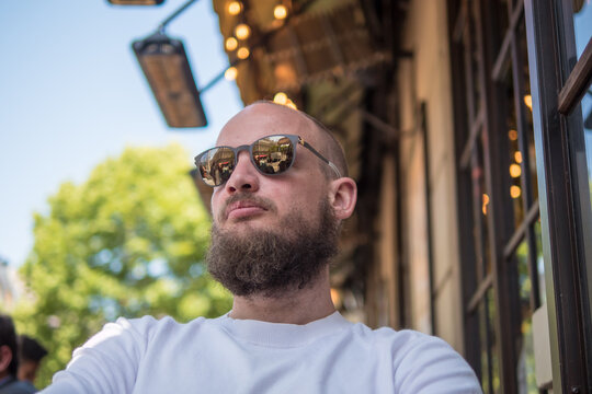 Handsome French bearded man with fashionable sunglasses sitting on a cafe terrace in Paris