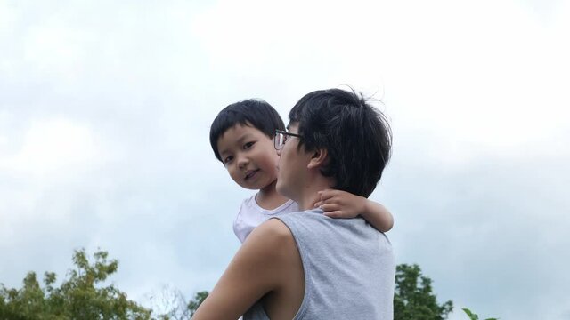 Authentic asian cute child boy in hug of father pointing finger to sky. Kid and dad in happy moment outdoor. Concept of family activity, father day, togetherness, relationship, love, future, education