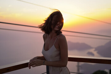 Young woman in a silk light dress at a magnificent sunset on the top of a mountain overlooking the ski lifts in a romantic mood