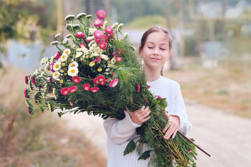 Happy girl walking on the road with flowers in her hands smiling closing her eyes