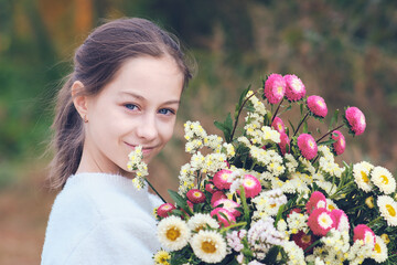 Happy teenage girl in a forest glade holding a huge bright bouquet of flowers in her hands.
